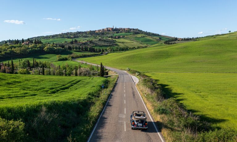 Scenic road through Tuscany wine country with vineyards and hilltop village, illustrating a DIY wine tour in Tuscany.